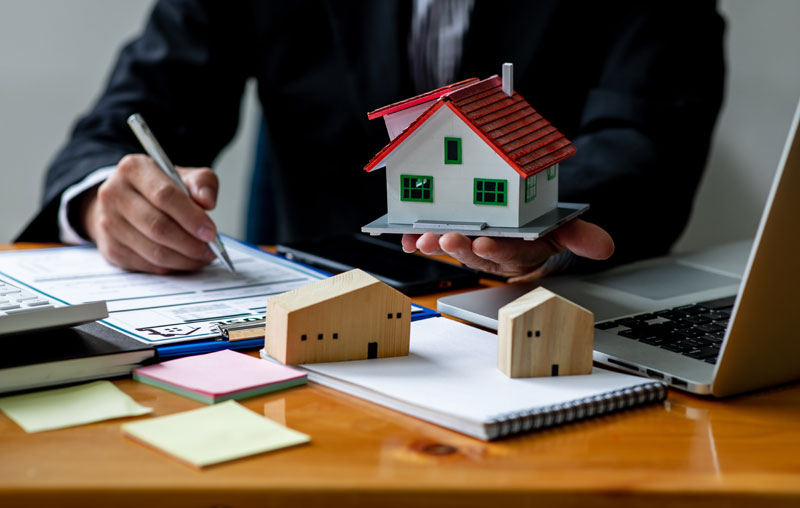 A lawmaker writes on a pad while holding a small replica of a house.